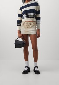 Pull en maille rayé bleu marine et crème, mini-jupe en denim beige avec ceinture, sac à main noir, chaussettes blanches, chaussures noires épaisses.