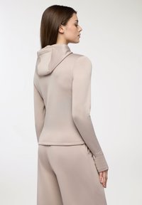 Felpa beige aderente realizzata in tessuto morbido, con colletto alto, maniche lunghe e design elegante, abbinata a pantaloni coordinati.