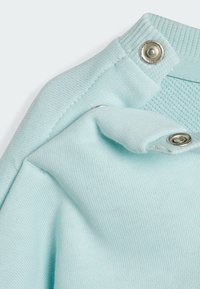 Light blue cotton fabric, textured with ribbed collar and snap closures. Smooth surface with a subtle pattern, showcasing a folded design.
