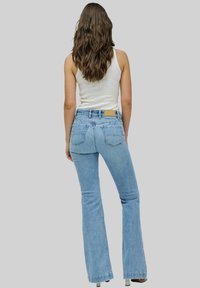 Jeans de campana de color azul claro con una cintura alta, que presentan un diseño clásico de cinco bolsillos y una etiqueta de cuero marrón en la parte posterior de la cintura.