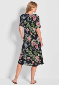 Robe à manches courtes à motifs floraux présentant un fond noir avec des roses roses et bleues ainsi que des feuilles vertes. Mi-longue avec un ourlet évasé.