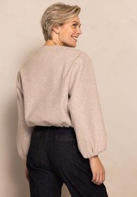 Light beige sweater with a relaxed fit, wide sleeves, and ribbed cuffs, paired with dark denim jeans featuring back pockets.