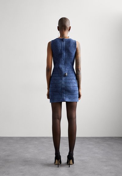 Denim mini kleita ar vertikālu ribota raksta, tumši zila krāsa, bez piedurknēm, aizmugurējais rāvējslēdzis un melnas augstpapēžu kurpes.