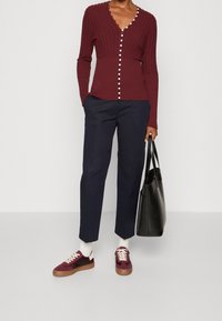 Viininpunainen ribbineulottu neuletakki V-kauluksella ja pyöreillä napeilla, yhdistetty laivastonsinisiin housuihin ja viininpunaisiin lenkkareihin. Asun täydentää musta olkalaukku.