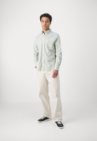 Light green, long-sleeve button-up shirt with a chest pocket, paired with white wide-legged pants and dark green sneakers.