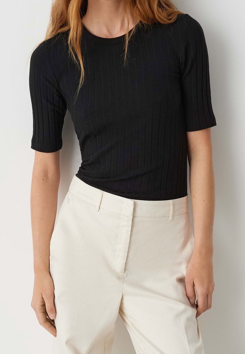 Haut noir à manches courtes côtelé avec un design ajusté. Porté avec un pantalon couleur crème, présentant une texture lisse et une coupe sur mesure.