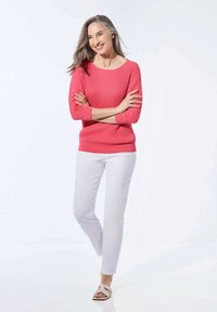Rippiger rosa Pullover mit langen Ärmeln, weißen, maßgeschneiderten Hosen und beigen Sandalen. Der Pullover hat einen runden Ausschnitt und ein strukturiertes Muster.
