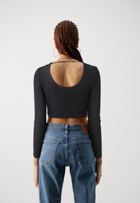 Must musta varrukatega crop top, millel on ümmargune seljaava, koos kõrge vöökohaga siniste teksadega, millel on klassikaline õmblus ja taskud.