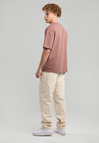 Ruskea pyöreäkauluksinen t-paita lyhyillä hihoilla, puuvillakangasta, rento malli, yhdistetty beigen värisiin leveälahkeisiin housuihin ja valkoisiin lenkkikenkiin. Minimalistinen muotoilu.