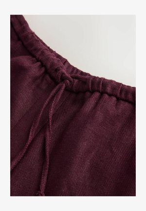 Prim-plan al unei benzi de talie din material textil mov închis, cu o bandă elastică și un șiret legat, pe un fundal simplu.