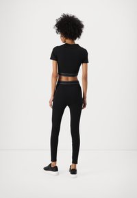 Fekete crop póló és magas derekú leggings texturált derékkal. Fekete sportcipővel párosítva, fehér talppal.