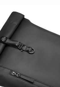 Fekete roll-top táska sima, vízálló anyagból, fényes felülettel. Egy nylon pánttal és csattal, valamint egy oldalsó cipzáras zsebbel rendelkezik.