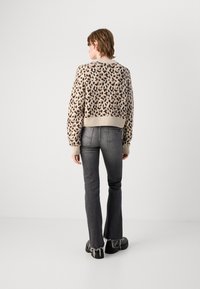 Beige, kurz geschnittenes Sweatshirt mit Leopardenmuster, gerippten Bündchen, kombiniert mit dunkelgrauen Schlagjeans mit ausgefranstem Saum und Gesäßtaschen.