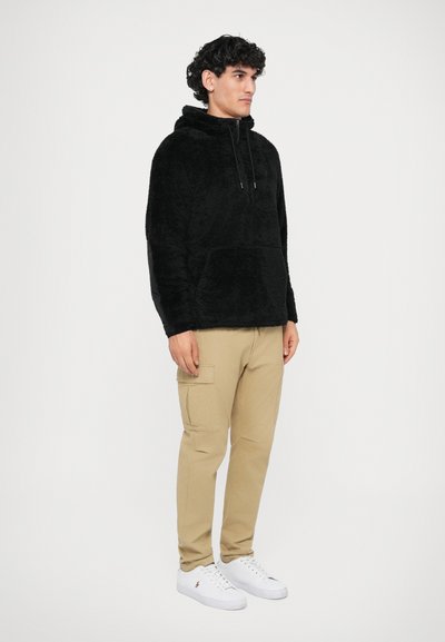 Hanorac din fleece negru cu buzunar tip kangur și cordon reglabil. Asortat cu pantaloni cargo bej și adidași albi.