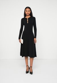 Čierne šaty s dlhými rukávmi, s priliehavým telo a rozšírenou sukňou, s detailmi gombíkov pri výstrihu a hladkou textúrou látky.