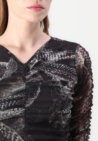 Svarte mønstrede bluser med V-hals, lange gjennomsiktige ermer og strukturert stoff med en blanding av slange- og abstrakte design.