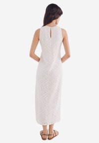 Abito maxi bianco in pizzo con motivi geometrici, design senza maniche, dettaglio con apertura a chiave sul retro e sandali flat. Tessuto liscio, silhouette aderente.
