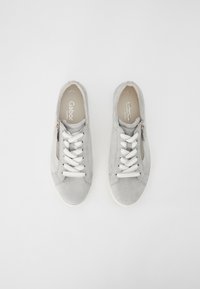 Harmaat mokkanahka tennarit valkoisilla nauhoilla, sivuvetoketjuyksityiskohtia, pyöristetty kärki ja teksturoitu pinta. Valkoinen kumipohja. Brändin logo sisäpohjassa.