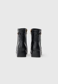 Botas de cano curto em couro preto com um bico arredondado, um salto bloco baixo e um fecho lateral. Apresentam hardware minimalista e uma textura suave.