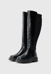 Bottes noires à hauteur de genoux avec une tige en cuir lisse, une semelle en caoutchouc texturé et des détails de couture discrets. Le design allie fonctionnalité et esthétique.