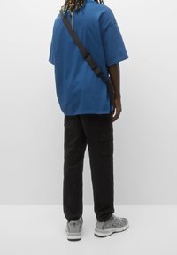Blaues übergroßes T-Shirt, schwarze Cargo-Hosen und graue Sportschuhe. Das T-Shirt hat eine glatte Textur, während die Hosen mehrere Taschen besitzen.