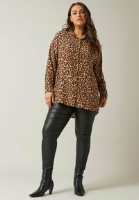 Camisa de estampado de leopardo con botones, mangas largas y un ajuste holgado, combinada con pantalones de cuero negro ajustados y botas de tobillo puntiagudas.