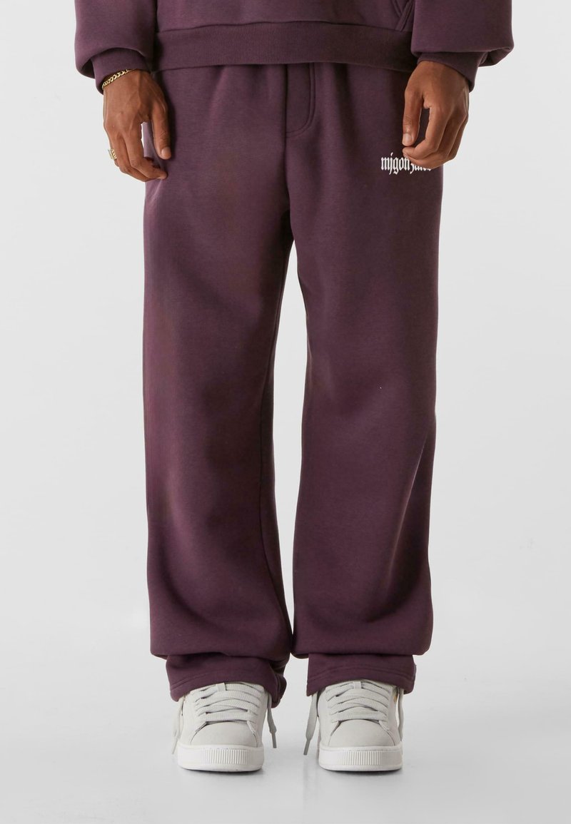 Lila Sweatpants mit lässiger Passform, ausgestattet mit Fronttaschen und einem kleinen Logo-Akzent auf dem linken Oberschenkel. Kombiniert mit weißen Sneakern.
