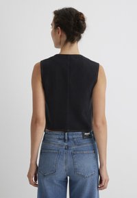 Schwarzes Denim-Ärmelloses Oberteil mit hohem Halsausschnitt, kombiniert mit hellblauen, hochtaillierten Jeans mit dezenten Nähten und Gesäßtaschen.