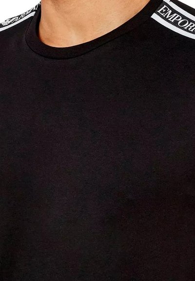T-shirt noir à col rond, avec des accents de logo blanc sur l'épaule. Texture lisse avec un design ajusté.