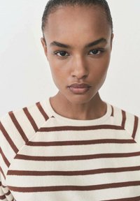 Striped crewneck sweater made of soft fabric; features beige with horizontal brown stripes and raglan sleeves.