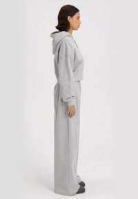 Grijze cropped hoodie met lange mouwen gecombineerd met high-waisted, wijde broek. Zachte, gestructureerde stof met een losse pasvorm en capuchon-detail.