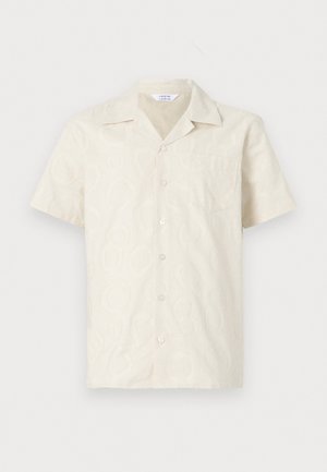 Camisa de manga curta em creme com um padrão discreto, com botões à frente e um bolso no peito. Feita de um tecido leve.