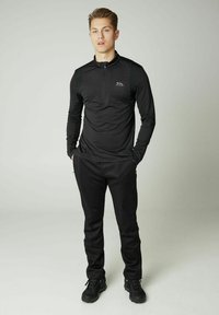Schwarzes Sportoberteil mit einem Viertel-Reißverschluss und Berglogo, kombiniert mit schwarzen Hosen. Glatte Textur, figurbetontes Design und lange Ärmel.
