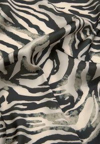 Čierno-biely zebrový vzor na látke s hladkou textúrou, obsahujúci výrazné pruhy a jemné, rozpité okraje, elegantne poskladaný do jemných záhybov.