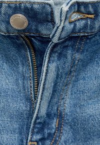 Jean en denim avec un lavage bleu, doté d'un bouton-pression en métal et d'une fermeture éclair. Coutures contrastées visibles le long des coutures, avec une texture lisse.