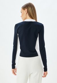 Maglione a maniche lunghe con design a blocco di colore blu navy e bianco, realizzato in tessuto morbido. Silhouette aderente con scollatura rotonda e texture a coste.