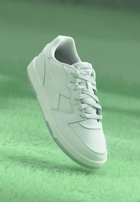 White leather sneaker with perforated toe, flat laces, and grey rubber sole. Featured brand logo on tongue and side panel.