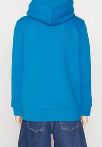 Sudadera azul con capucha de textura suave, mangas con puños y un corte relajado, complementada con jeans de mezclilla oscura.