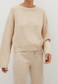 Béžový žebrovaný pletený svetr s kulatým výstřihem, oversized rukávy a zkráceným designem. Měkká textura, doplněná o odpovídající svetle béžové kalhoty.