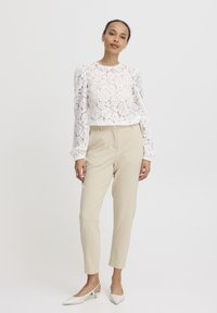 Hvid blonder langærmet top parret med beige tapered bukser og hvide spidse hæle. Fremtrædende blomsterblonde mønster og smockede ærmer.