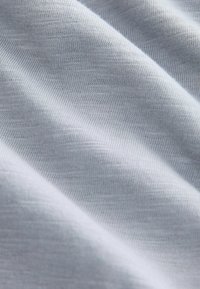 Tela de color gris claro con una textura suave y lisa. Presenta un patrón de punto fino, que exhibe sutiles variaciones de tono en toda la superficie.