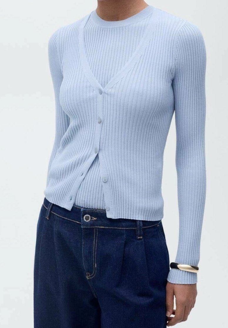 Personne portant un cardigan côtelé bleu clair sur un top à manches longues assorti et un pantalon taille haute bleu foncé avec un bracelet au poignet gauche.