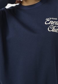 Granatowa bluza z okrągłym dekoltem, wykonana z miękkiego materiału. Posiada białe haftowane napisy "GOOD Energy Club" na piersi.