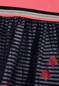 Rosa topp med en lager av marinblå tyllkjol som har horisontella ränder och röda stjärnmönster. Inkluderar silver- och svarta accentband.