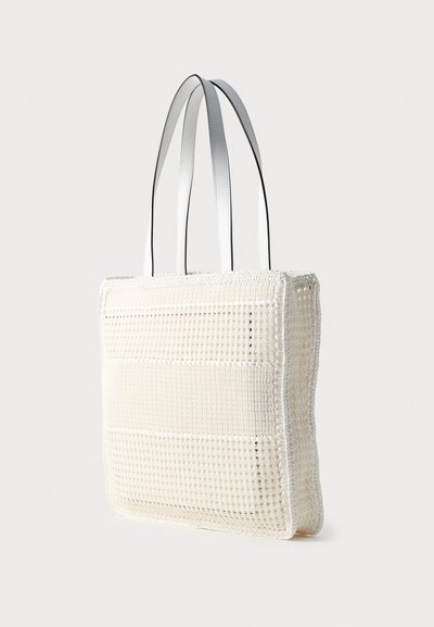 Sac cabas blanc tissé avec deux longues anses blanches lisses, forme rectangulaire et texture à petit motif carré.