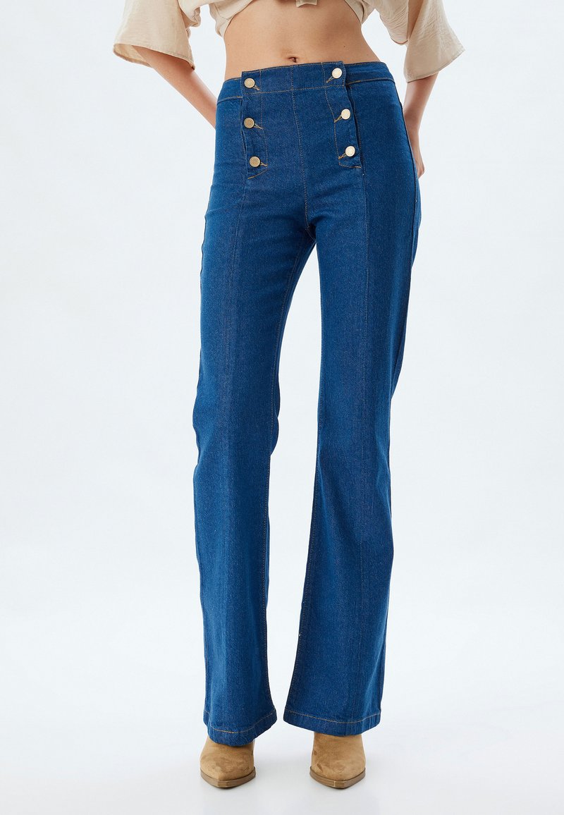 Los pantalones acampanados de mezclilla azul de cintura alta presentan un cierre frontal con botones, costuras en contraste y una textura suave.