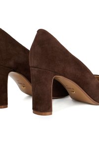 Pair of dark brown suede block-heeled shoes with closed backs and rounded toes on a white surface.