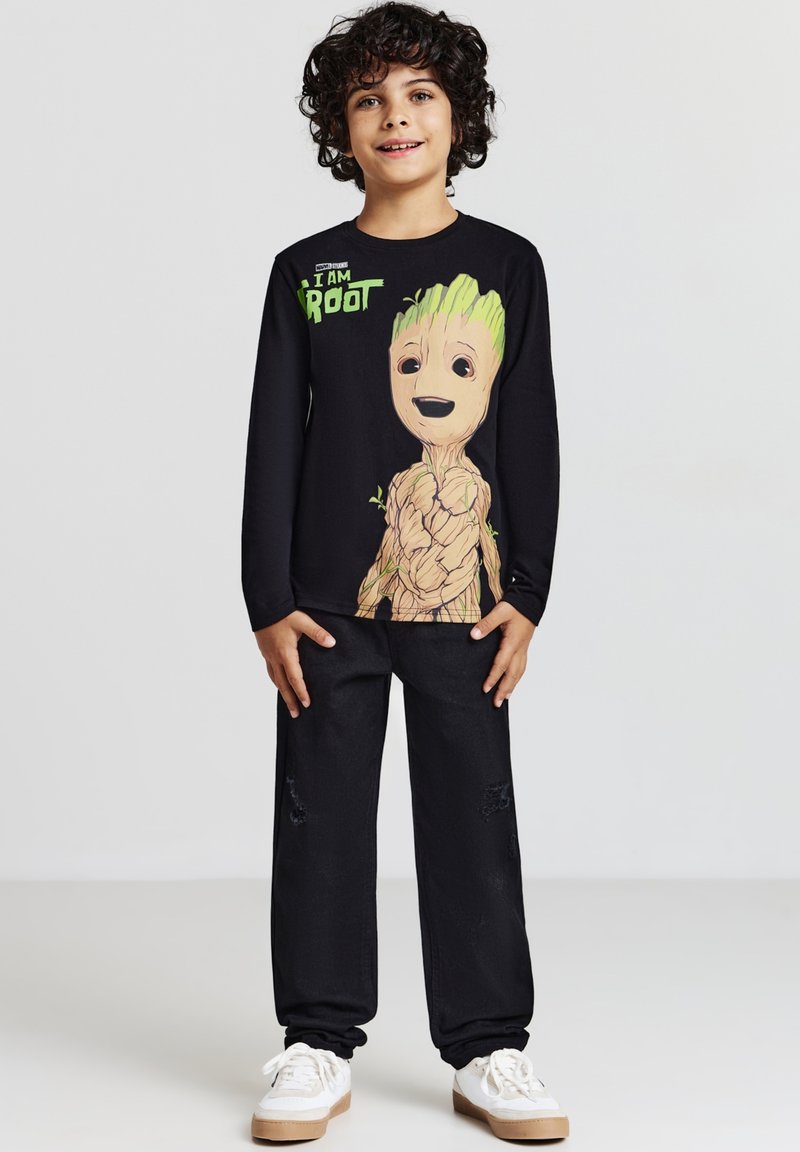 Maglietta nera a maniche lunghe con una grande grafica di Groot e accenti verdi, abbinata a pantaloni neri e sneakers bianche.