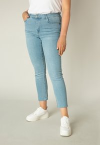 Lichtblauwe katoenen skinny jeans met een rafelige zoom, voorzakken en knoopsluiting, gecombineerd met witte sneakers. Gladde textuur en slim fit ontwerp.