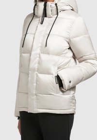 Chaqueta de invierno acolchada en gris claro. Cuenta con capucha, cierre de cremallera y cordones negros. Incluye bolsillos laterales y un acabado texturizado.